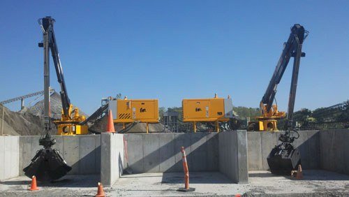 Two stationary mount loaders with clamshell buckets at a material bin